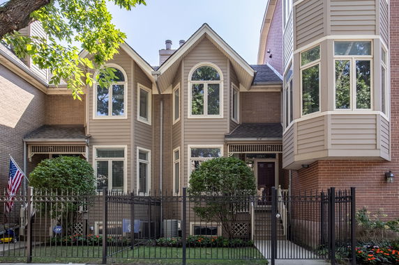 Front view of a multi-story townhouse with bay windows and a fenced yard.