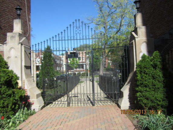 Metal gate with brick pillars and pathway leading to residential area.
