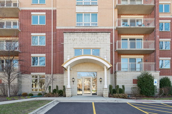 Front view of a multi-story brick apartment building with balconies and an arched entrance.