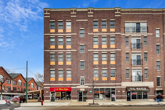 Front view of a multistory brick building with ground floor shops.