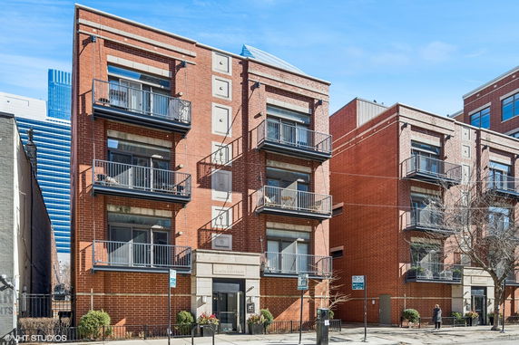 Front view of a three-story brick apartment building with balconies.