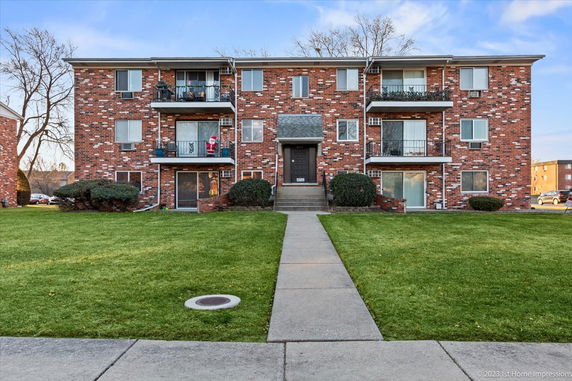 Front view of a three-story brick apartment building with balconies.