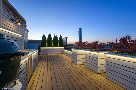 Rooftop with wooden decking and planters, featuring ambient lighting.