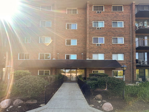 Front view of a multi-story brick apartment building with a central entrance.