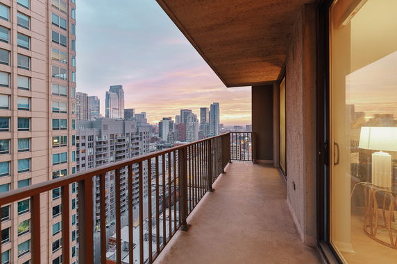 Balcony view overlooking a city skyline at sunset with tall buildings in the background.