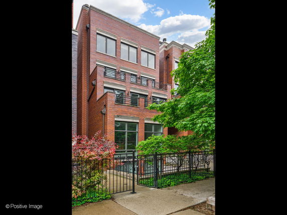 Front view of a multi-story brick building with large windows and a metal fence.