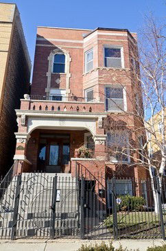 Front view of a three-story brick house with architectural details and a fenced entrance.