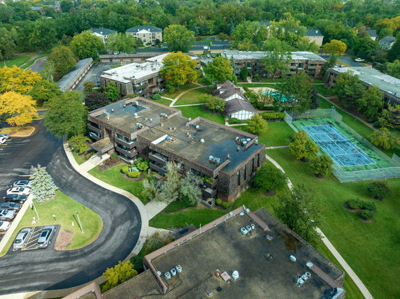 Aerial view of a residential complex with multiple buildings, green lawns, and a tennis court.