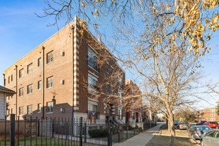 Side view of a multi-story brick building with large windows and a fenced area.