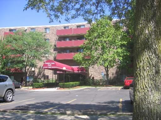 Front view of a multi-story residential building with red balcony railings and an entrance canopy.