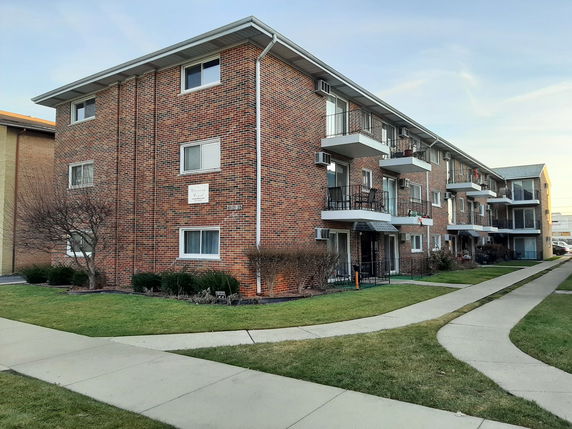 Front view of a multi-story brick apartment building with balconies.
