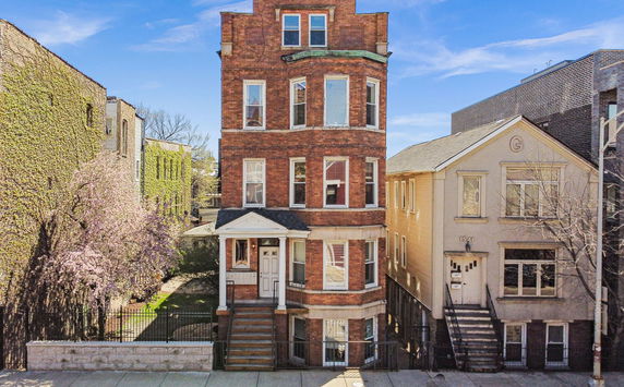 Front view of a multi-story brick building with bay windows and a porch entrance.