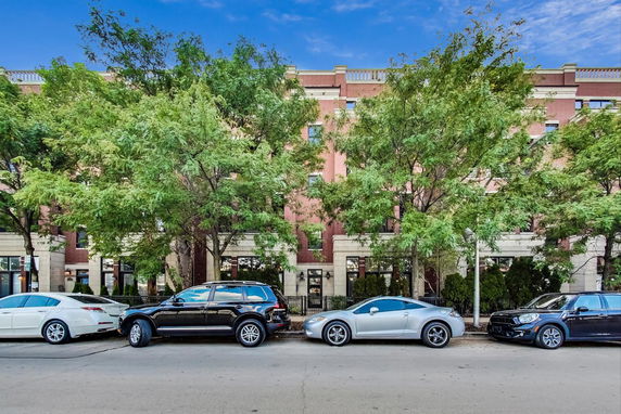 Front view of a multi-story brick building with trees and parked cars.