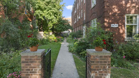 Pathway leading through a garden area between two brick buildings.