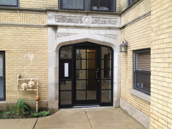 Front view of a brick building entrance with an ornate stone archway and glass door.