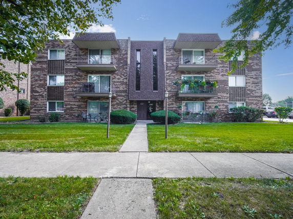 Front view of a three-story brick apartment building with balconies.