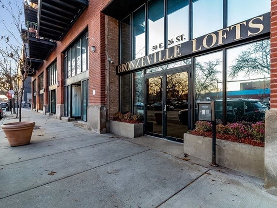 Front view of a building labeled as Bronzeville Lofts with large glass doors and red brick exterior.