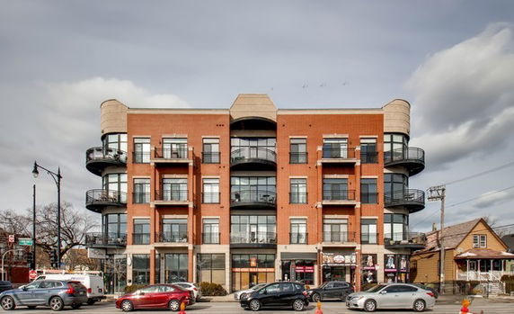 Front view of a four-story brick building with balconies and storefronts.