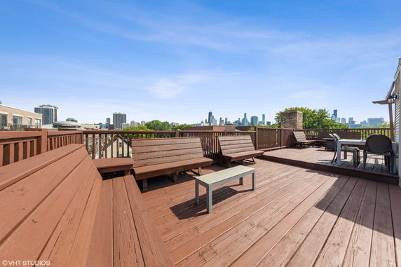 Wooden rooftop deck with benches and a table, featuring a skyline view in the background.