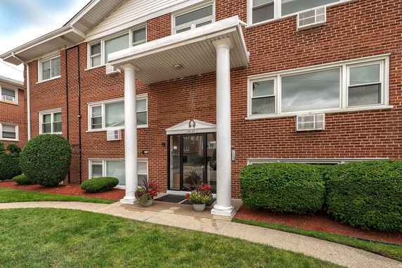 Front view of a brick apartment building with white pillars and multiple windows.