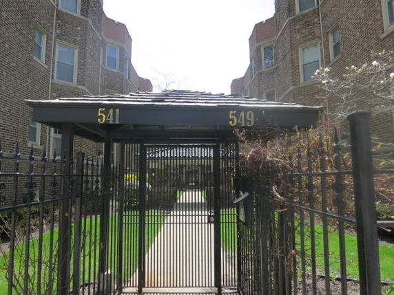 Front view of a multi-story brick apartment building with gated entrance.