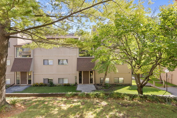Front view of a multi-story residential building with an entrance path and surrounding trees.