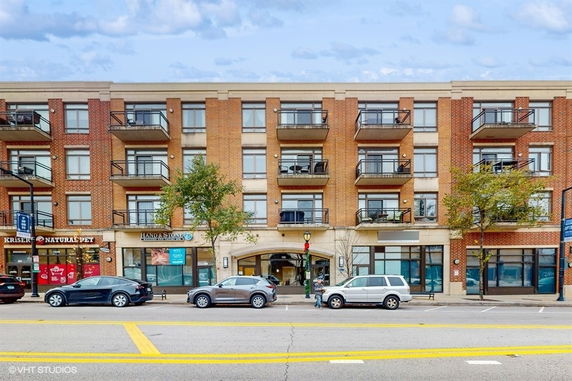 Front view of a multi-story apartment building with balconies and ground-level retail shops.
