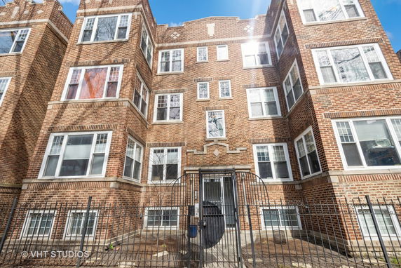Front view of a multi-story brick building with numerous windows and a gated entrance.