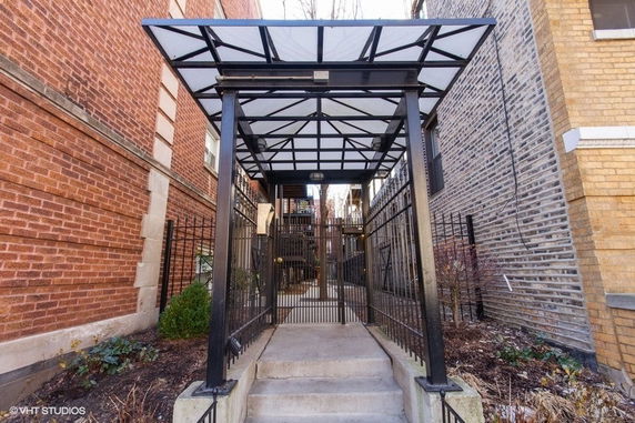Entrance view of a gated walkway between two brick buildings with a covered metal structure.