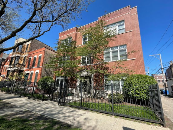 Front view of a three-story brick building with a fence in front.
