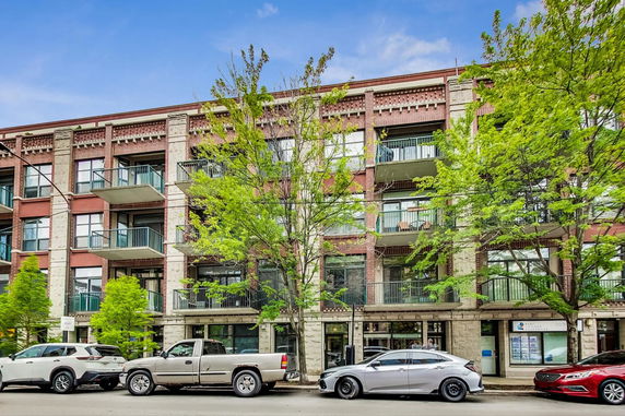 Front view of a multi-story residential building with balconies and trees in front.