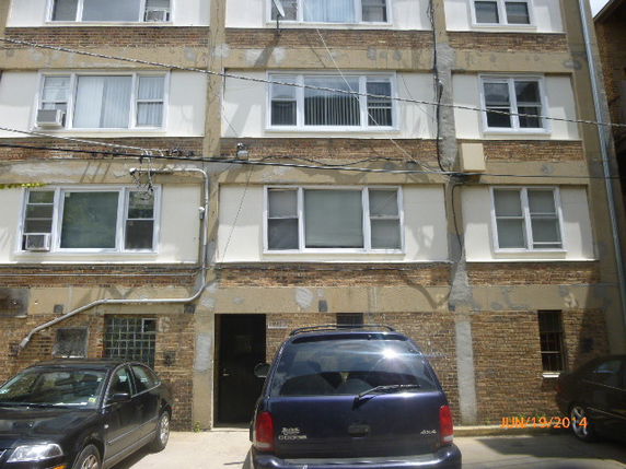 Front view of a multi-story building with multiple windows and parked cars.