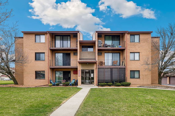 Front view of a three-story brick apartment building with balconies.