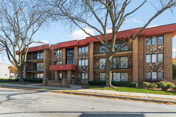 Front view of a three-story brick building with a red roof and balconies.