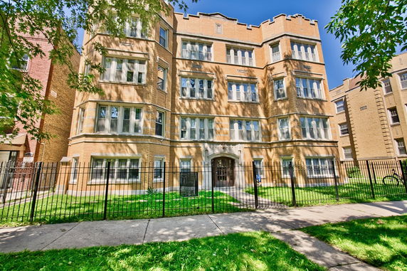 Front view of a multi-story brick building with numerous windows and a gated entrance.