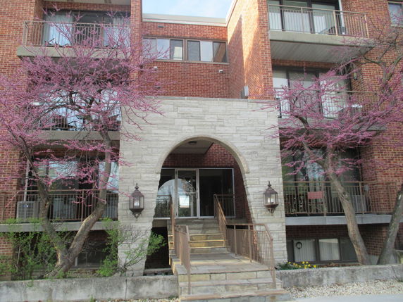 Front view of a brick apartment building with balconies and an arched entrance.