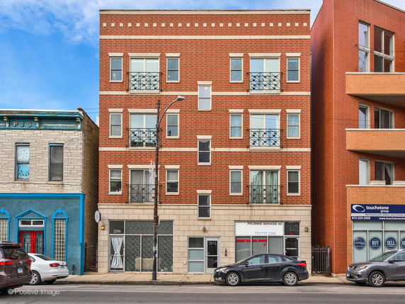 Front view of a multi-story brick building with multiple windows and metal railings.