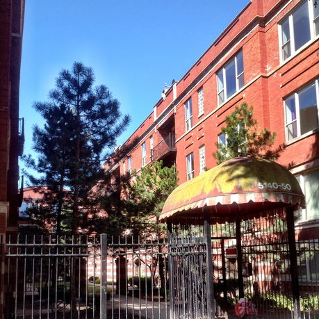 Front view of a multi-story brick building with an entrance canopy and surrounding trees.