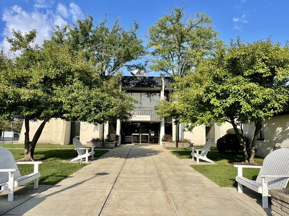 Front view of a two-story building with a pathway and trees lining the entrance.