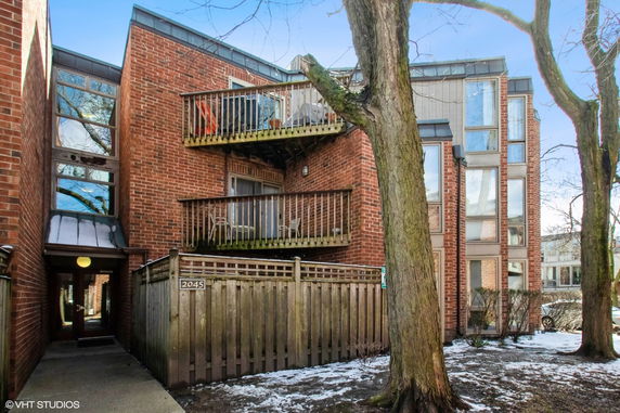 Front view of a multi-story brick building with balconies and a wooden fence.