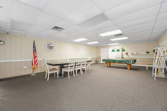 Room with a long dining table, chairs, a covered pool table, and an American flag in the corner.