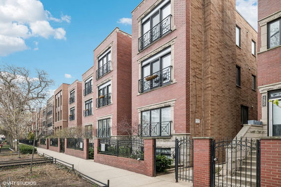 Front view of a brick multi-story apartment building with black railings.