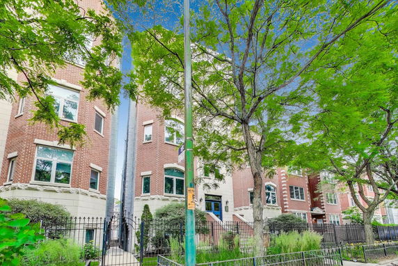 Front view of a multi-story brick apartment building with large windows and a gated entrance.
