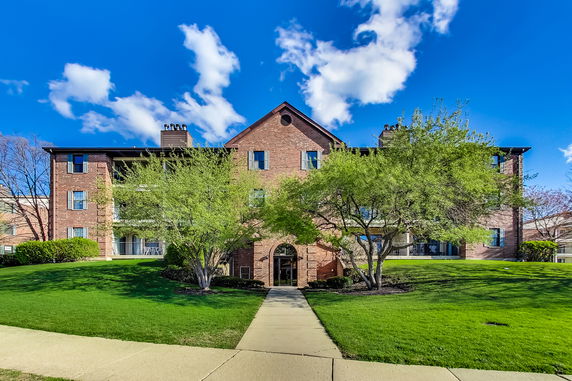 Front view of a three-story brick building with multiple chimneys and landscaped entrance.