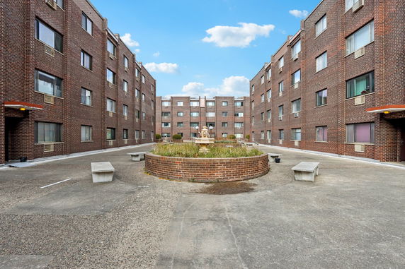 Front view of a multi-story brick apartment building with adjacent structures and a central courtyard.