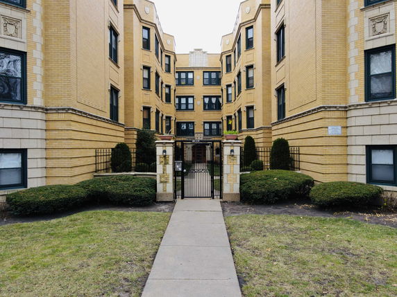 Front view of a multi-story brick apartment building with gated entrance.