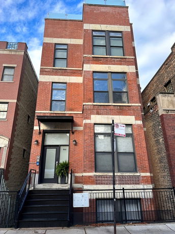 Front view of a three-story brick building with large windows and a metal staircase leading to the entrance.