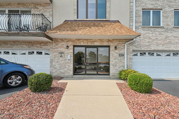 Front view of a multi-story brick building entrance with two garage doors and a walkway.