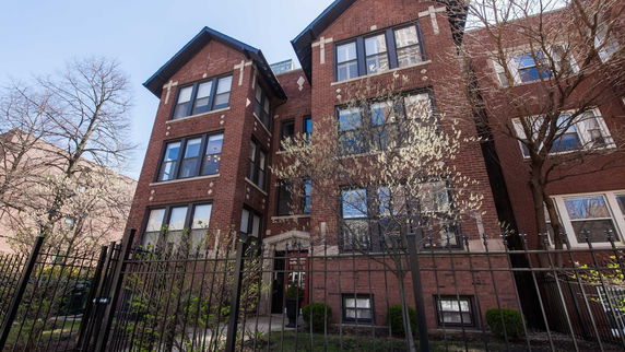 Front view of a multi-story brick building with a gabled roof and several large windows.