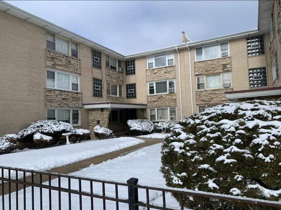 Front view of a three-story apartment building with snow-covered shrubs.